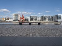 an empty bench sitting on the side of a river with buildings in the background and water behind