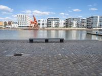 an empty bench sitting on the side of a river with buildings in the background and water behind