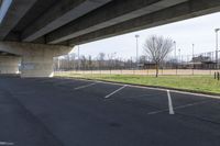 an empty parking lot with cars driving under an overpass or abovepass of the highway