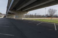 an empty parking lot with cars driving under an overpass or abovepass of the highway