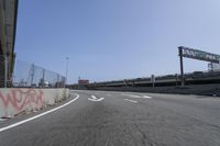 the view of a highway with graffiti and road markers along it and a pedestrian bridge in the background