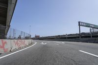 the view of a highway with graffiti and road markers along it and a pedestrian bridge in the background