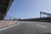 the view of a highway with graffiti and road markers along it and a pedestrian bridge in the background