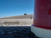 two people walking next to a lighthouse on a beach with a ramp leading to it