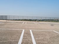 empty parking spaces with fenced in view of city skyline in the distance, during summer