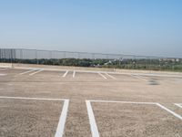 empty parking spaces with fenced in view of city skyline in the distance, during summer