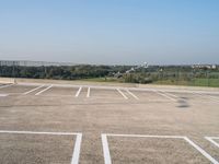 empty parking spaces with fenced in view of city skyline in the distance, during summer