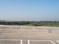 empty parking spaces with fenced in view of city skyline in the distance, during summer