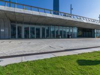 a large building with glass windows and lots of grass in front of it and a large brick walkway to the entrance