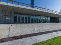 a large building with glass windows and lots of grass in front of it and a large brick walkway to the entrance