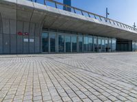 a large building with glass windows and lots of grass in front of it and a large brick walkway to the entrance