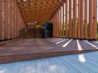 a walkway with wooden poles and a bench underneath them on a sunny day in a park