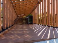 a walkway with wooden poles and a bench underneath them on a sunny day in a park