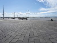 several benches are standing on the stone area near the ocean under a sky with white clouds