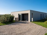 an enclosed building with doors and gravel in the front yard with lawn and bushes in front