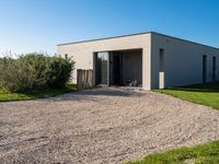 an enclosed building with doors and gravel in the front yard with lawn and bushes in front