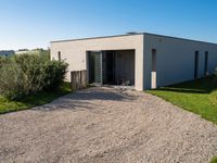 an enclosed building with doors and gravel in the front yard with lawn and bushes in front