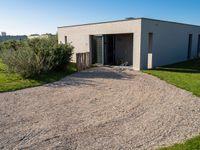 an enclosed building with doors and gravel in the front yard with lawn and bushes in front