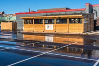 a wet car parking lot full of a small wooden building with a sign attached to it's roof