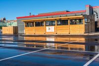 a wet car parking lot full of a small wooden building with a sign attached to it's roof