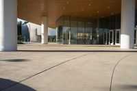 an empty courtyard has tall columns and a building that has glass doors and a metal frame around the door