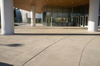 an empty courtyard has tall columns and a building that has glass doors and a metal frame around the door