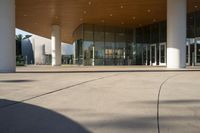 an empty courtyard has tall columns and a building that has glass doors and a metal frame around the door