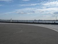 an empty concrete surface and a fence surrounding it with clouds in the sky in the distance