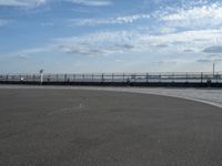 an empty concrete surface and a fence surrounding it with clouds in the sky in the distance