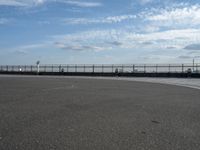 an empty concrete surface and a fence surrounding it with clouds in the sky in the distance