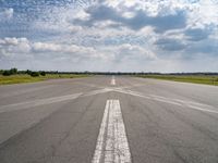 an airplane sits parked on an open runway with sky and clouds above it with lines running in between the road