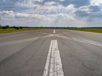 an airplane sits parked on an open runway with sky and clouds above it with lines running in between the road