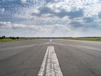 an airplane sits parked on an open runway with sky and clouds above it with lines running in between the road