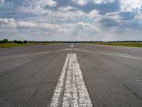 an airplane sits parked on an open runway with sky and clouds above it with lines running in between the road