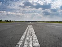 an airplane sits parked on an open runway with sky and clouds above it with lines running in between the road