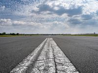 an airplane sits parked on an open runway with sky and clouds above it with lines running in between the road