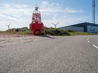 a red fire hydrant sitting on the side of a road near wind turbines and a building