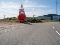 a red fire hydrant sitting on the side of a road near wind turbines and a building