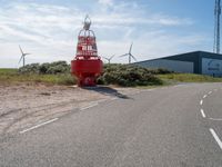 a red fire hydrant sitting on the side of a road near wind turbines and a building