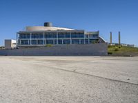 large industrial building with a glassy window overlooking the street and buildings below it as seen from an empty parking lot