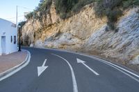 an empty street that looks like a narrow mountain road with three arrows pointing to the left