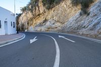 an empty street that looks like a narrow mountain road with three arrows pointing to the left