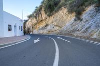 an empty street that looks like a narrow mountain road with three arrows pointing to the left