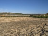 a large dirt field with fenced off land, with plane in the distance and sand flying by