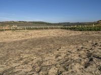 a large dirt field with fenced off land, with plane in the distance and sand flying by