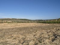 a large dirt field with fenced off land, with plane in the distance and sand flying by