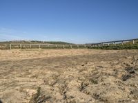 a large dirt field with fenced off land, with plane in the distance and sand flying by