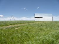 a large mirror building stands in a grassy field by a blue sky with white clouds