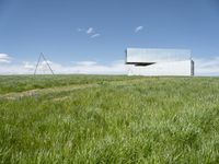 a large mirror building stands in a grassy field by a blue sky with white clouds