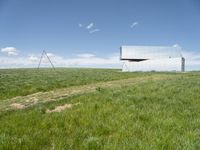 a large mirror building stands in a grassy field by a blue sky with white clouds